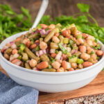 The bean salad in a white bowl with a spoon.