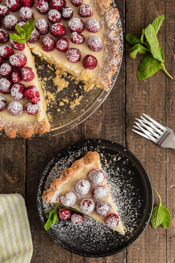 Raspberry crostata on a glass plate with a slice on a black plate.
