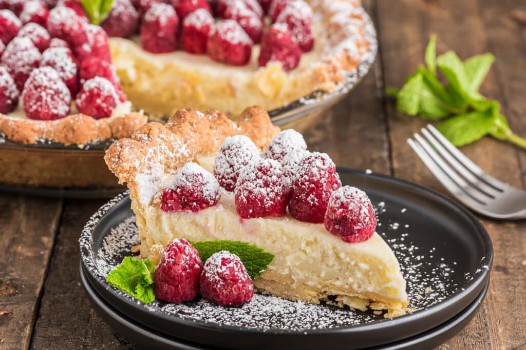 A slice of raspberry tart on a black plate.