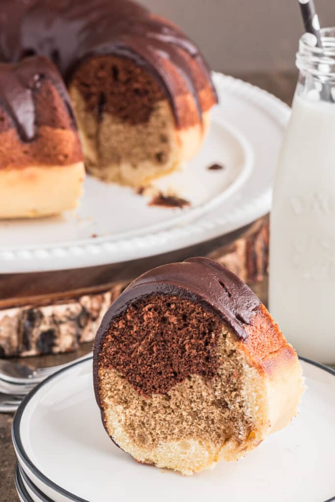 Bundt cake on a white stand with a slice on a white plate.