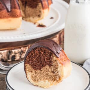 Bundt cake on a white stand with a slice on a white plate.