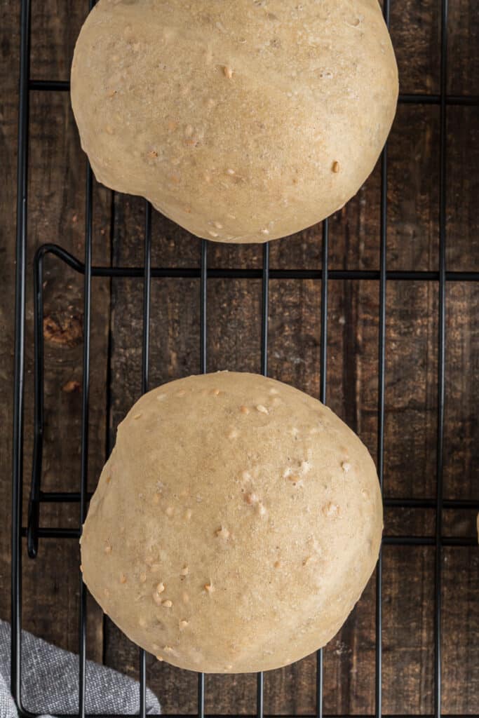 Two sesame buns on a wire rack.