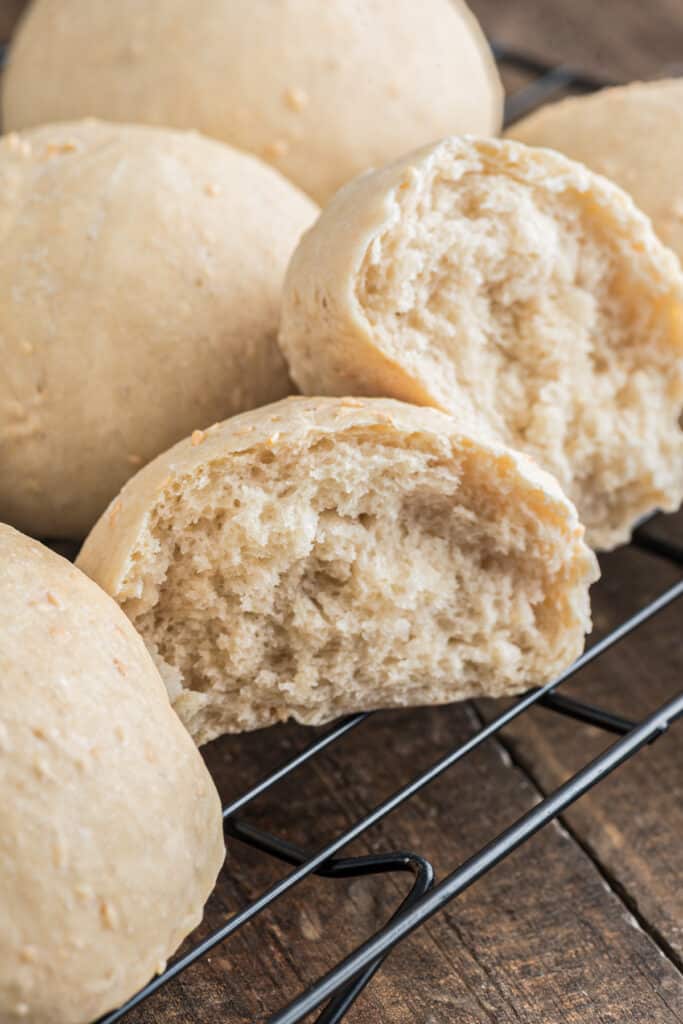 Sesame bread buns on a wire rack with one cut in half.