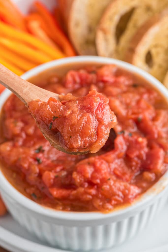 Tomato dip in a white bowl and some on a wooden spoon.