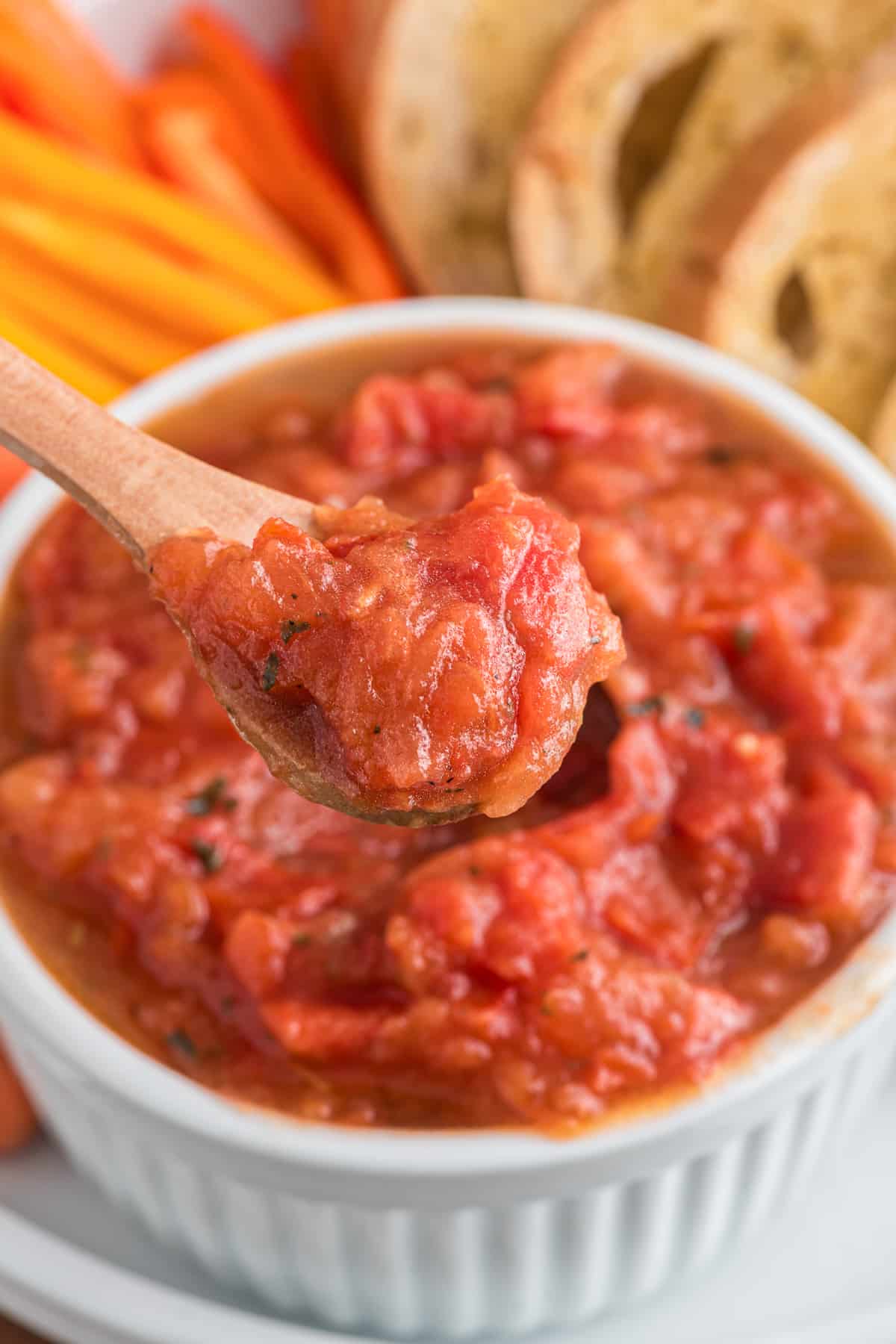 Tomato dip in a white bowl and some on a wooden spoon.