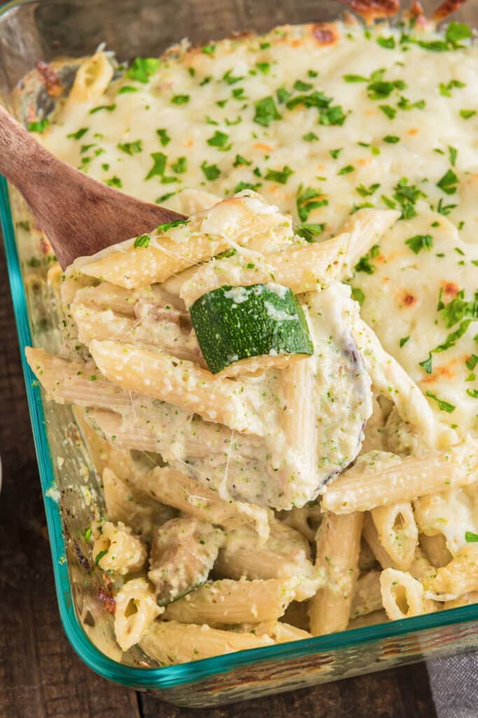Zucchini baked pasta in a glass pan on a wooden spoon.