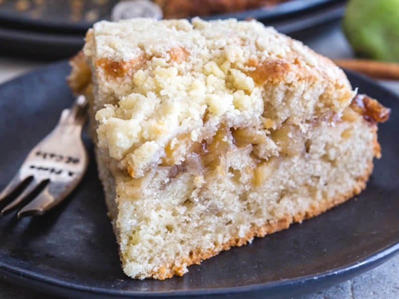 A slice of apple streusel cake on a black plate.