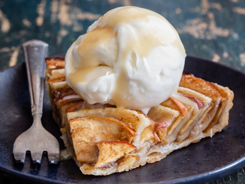 A slice of puff pastry apple pie with a scoop of ice cream.