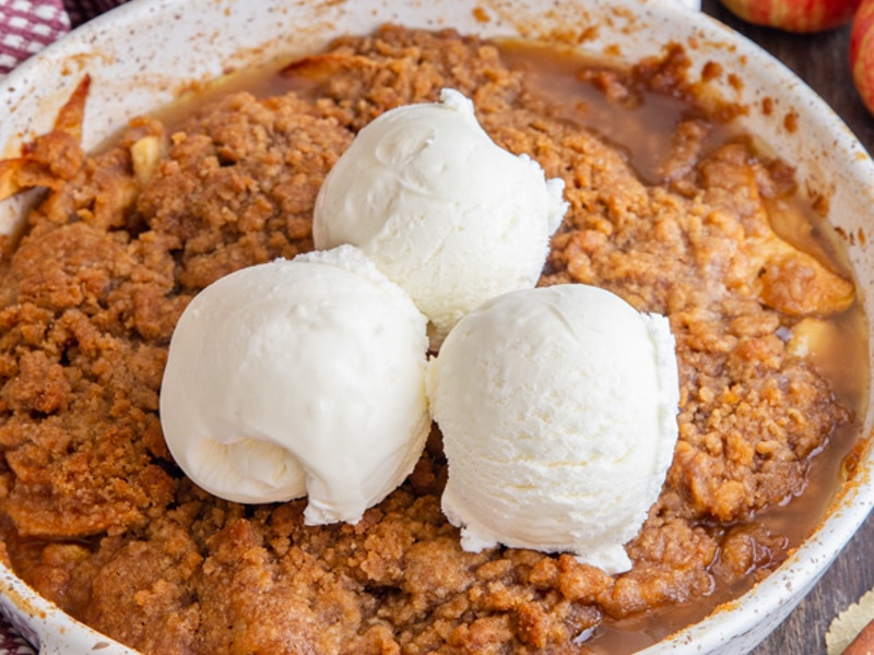 Apple crisp with three scoops of ice cream in a white pan.