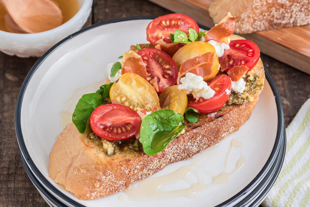 A prosciutto bruschetta on a white plate.