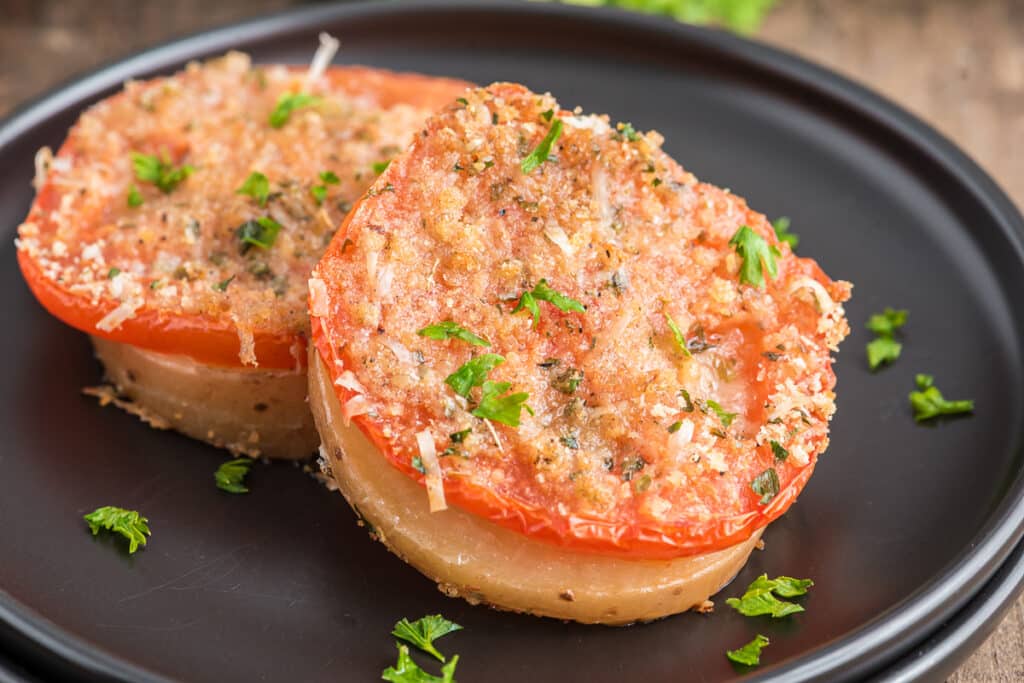 Two baked tomatoes on a black plate.
