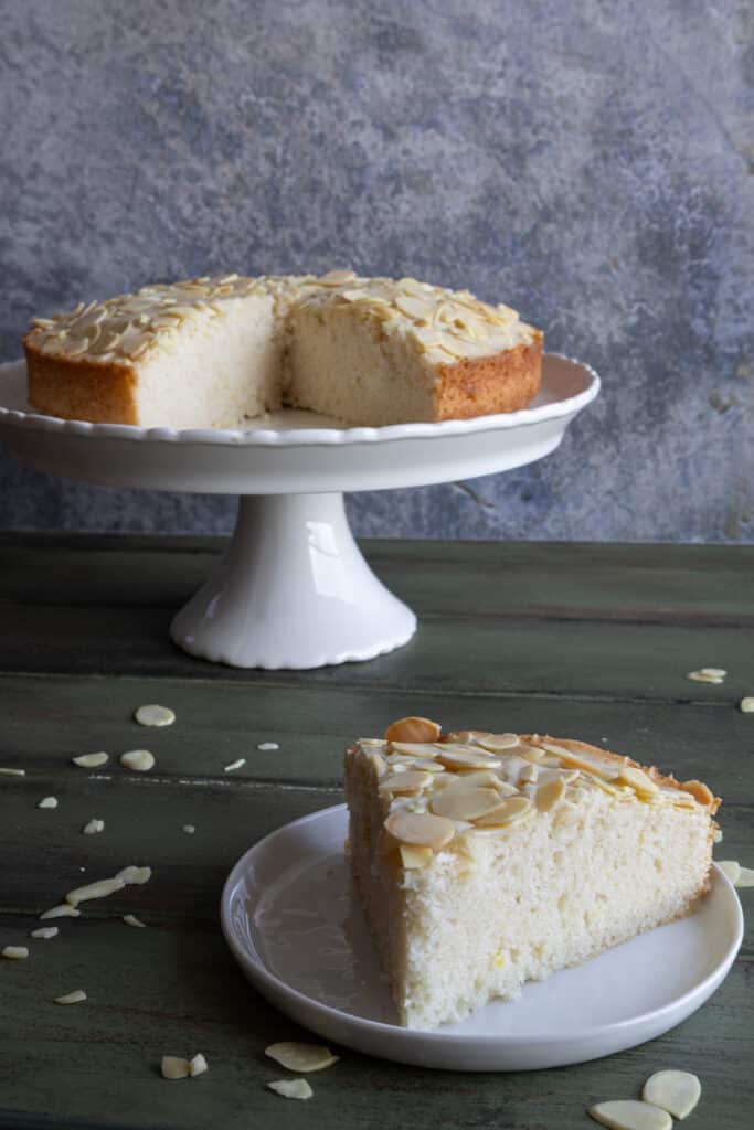 Almond cake on a cake stand with a slice on a white plate.