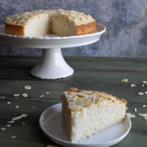 Almond cake on a cake stand with a slice on a white plate.