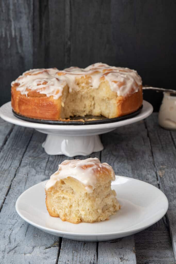 Cinnamon buns on a white plate stand with one on a white plate.