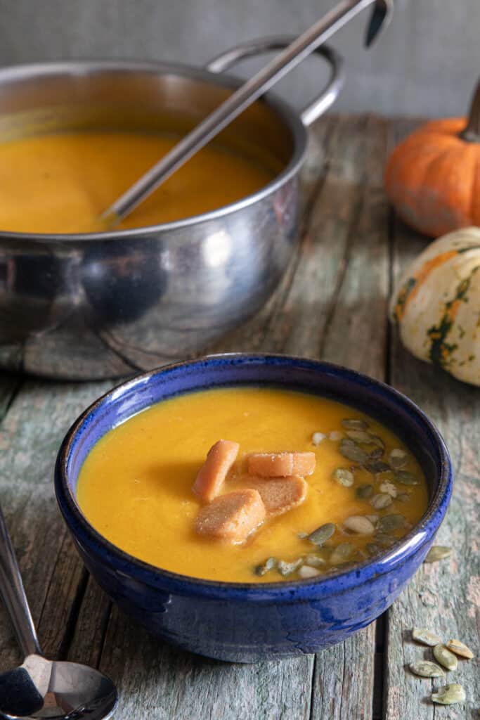 Squash soup in a silver pot and some in a blue bowl.