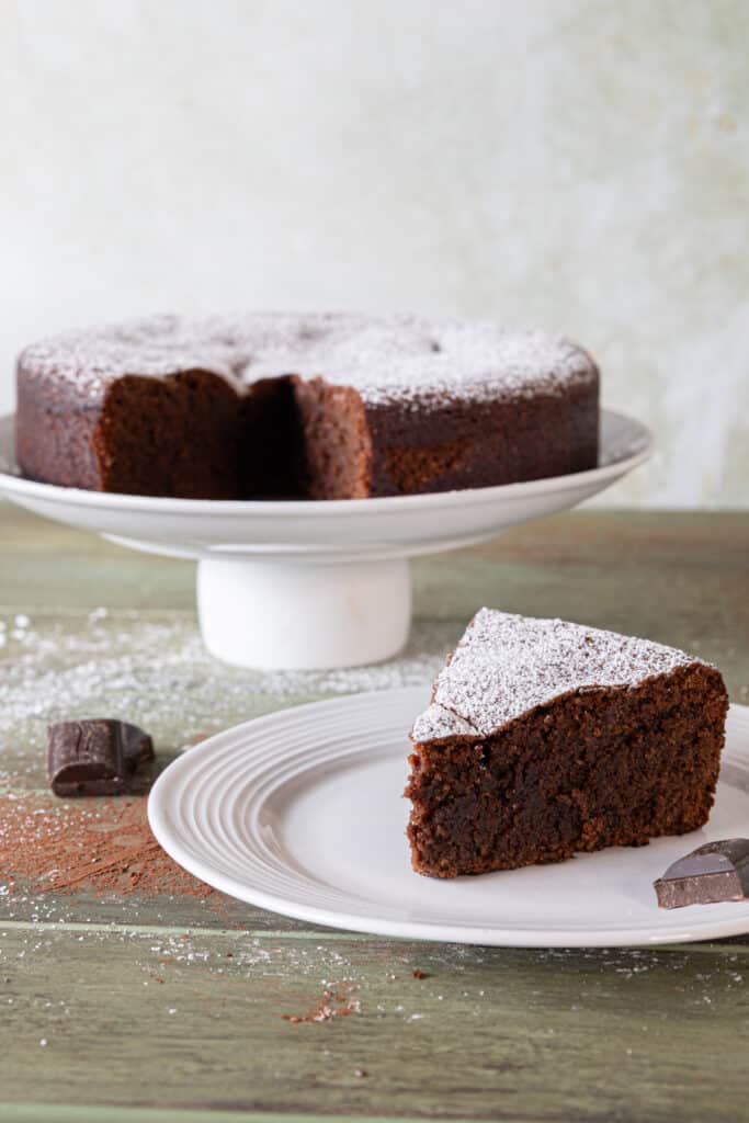 Chocolate caprese cake on a cake stand with a slice on a white plate.