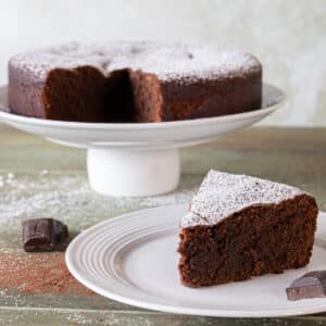 Chocolate caprese cake on a cake stand with a slice on a white plate.