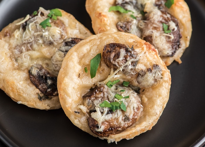 Mushroom puff pastry appetizers on a black plate.