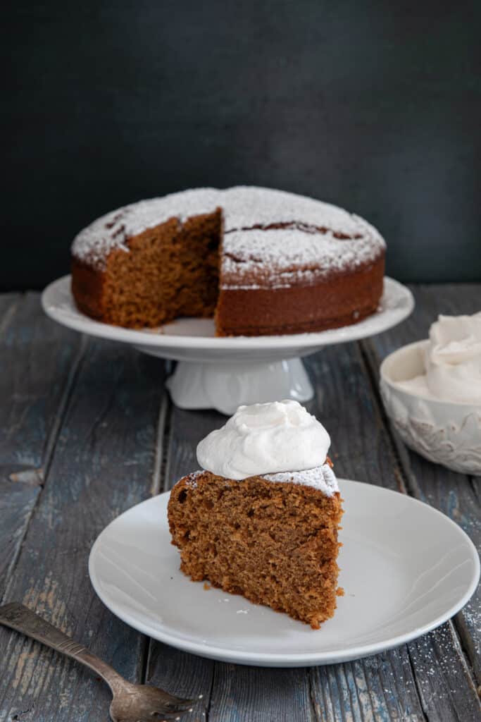 Cake on a cake plate and a slice on a white plate.