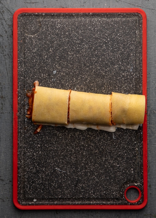 Rolling the pasta up nd cutting into three on the board.