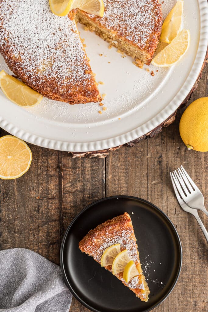 Lemon caprese cake on a white plate with a slice on a small black plate.