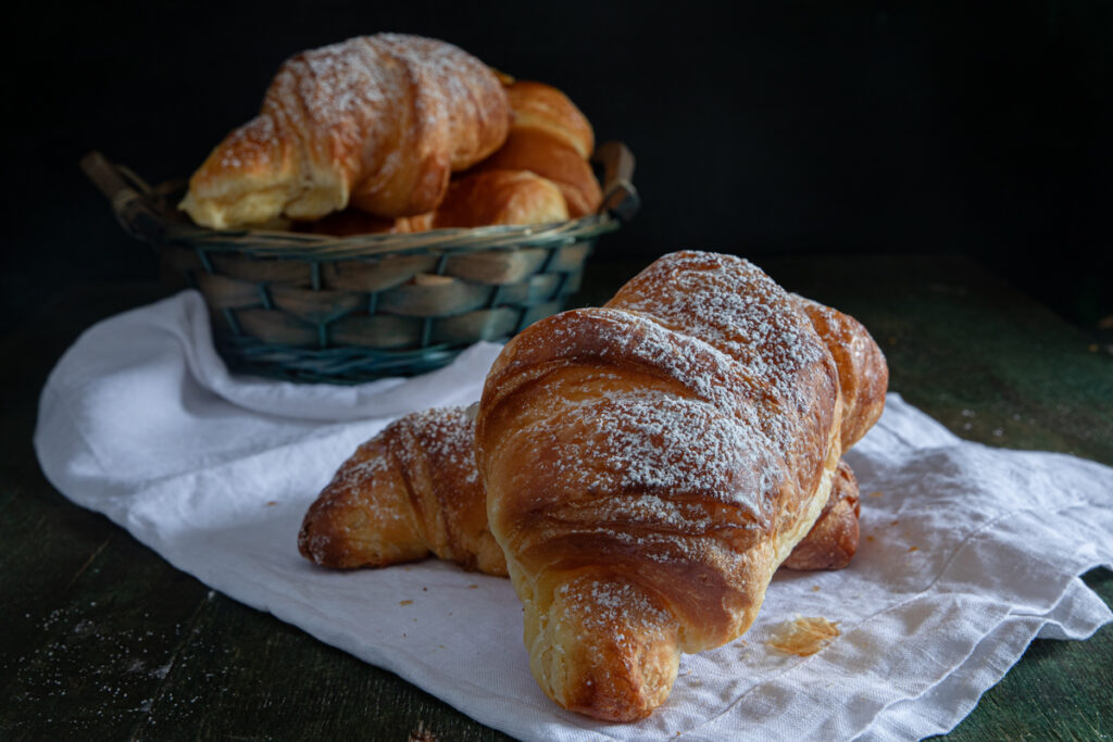 Cornetti in a basket and two on a white napkin.