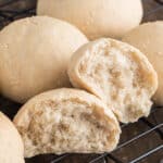 Sesame bread buns on a wire rack with one cut in half.