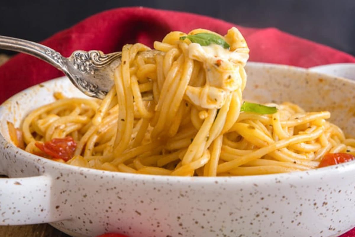 Hot caprese pasta with some on a fork in the pan.