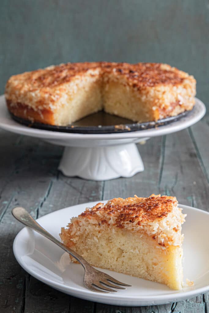 Lazy daisy cake on a cake stand with a slice on a white plate.
