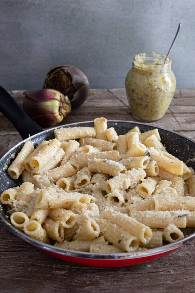 Pesto mixed with pasta in a red frying pan.