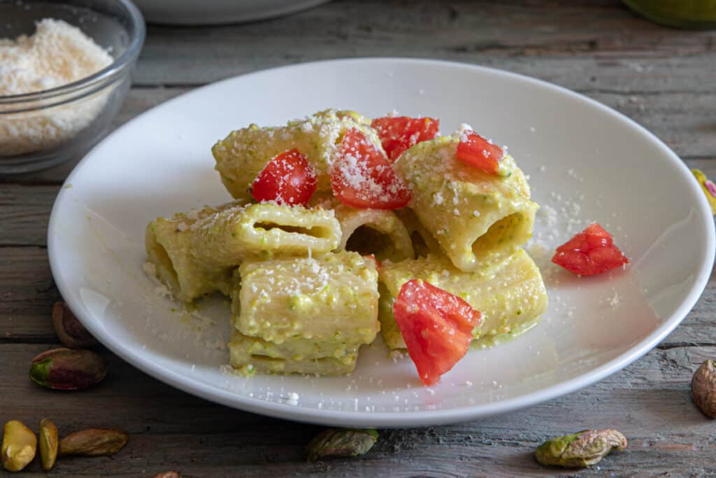 Pasta with pesto and tomatoes on a white plate.