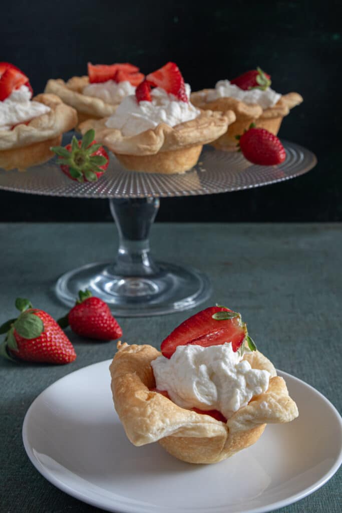 Cheesecake cups on a glass cake stand and one on a white plate.