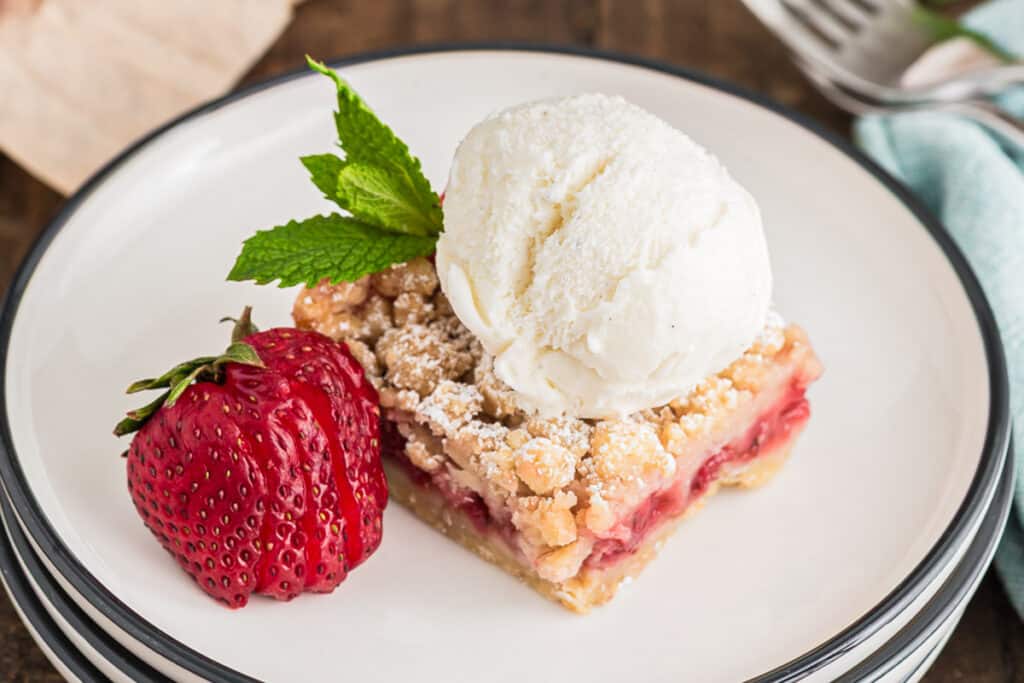 A crumb bar with a scoop of ice cream on a white plate.