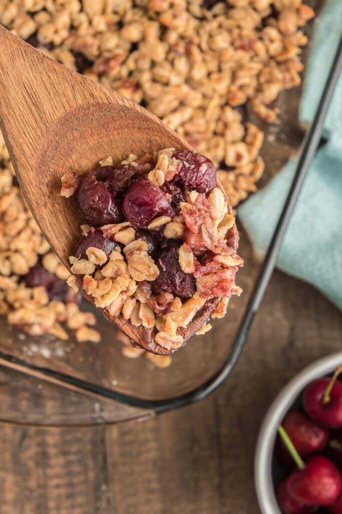 Some cherry crumble on a wooden spoon and in the glass pan.