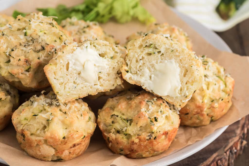 Muffins on a plate with one cut open with butter on it.