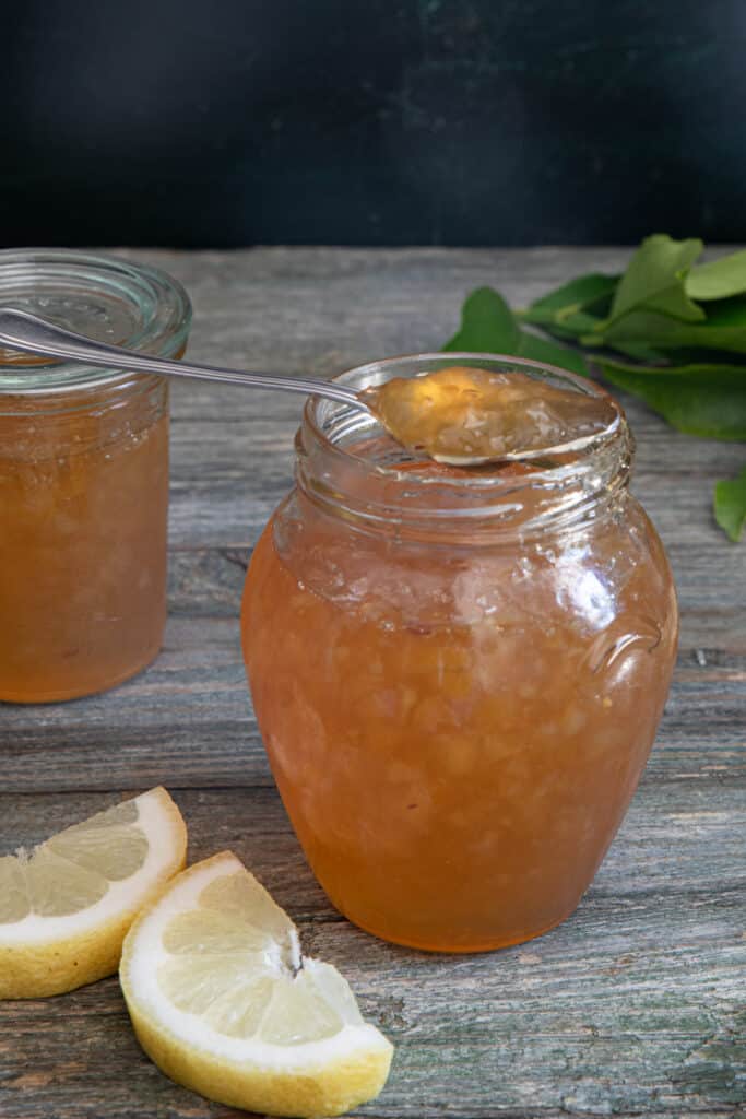 Marmalade in a two jars with some on a spoon.