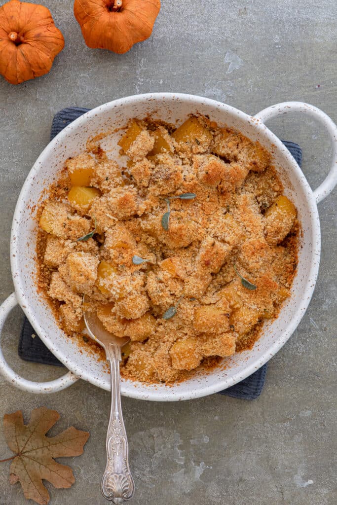 Squash gratin in a white dish with a spoon.