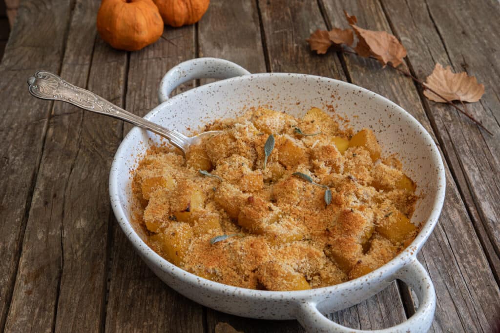 The squash gratin in a white baking dish with a spoon.