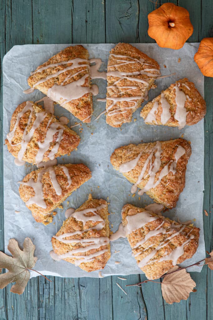 Frosted pumpkin scones on a piece of parchment paper.