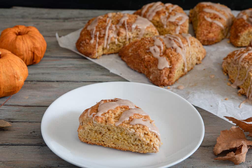 A scone on a white plate and some on parchment paper.